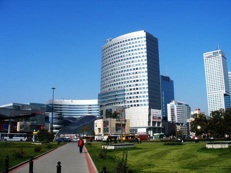 a city park with a paved walkway and green lawn, people walking in the distance