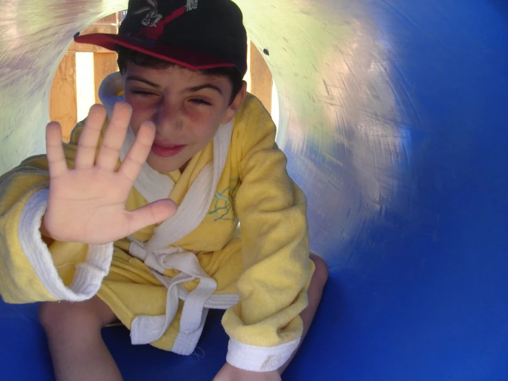 a young child who is sitting on the slide and waving with his hand up