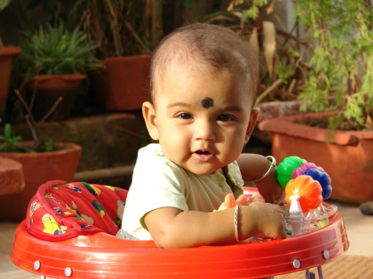 a young baby sitting in a plastic chair next to potted plants