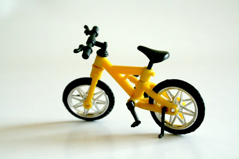 a yellow toy bicycle with a black seat and black spokes