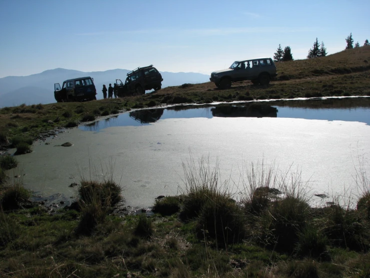 three off road trucks traveling over a hill in the sun