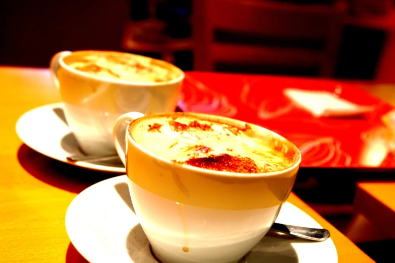 two coffee cups on white plates with spoons