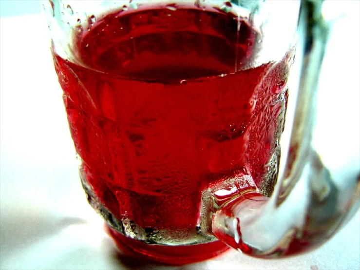 a glass filled with red liquid sitting on top of a white table
