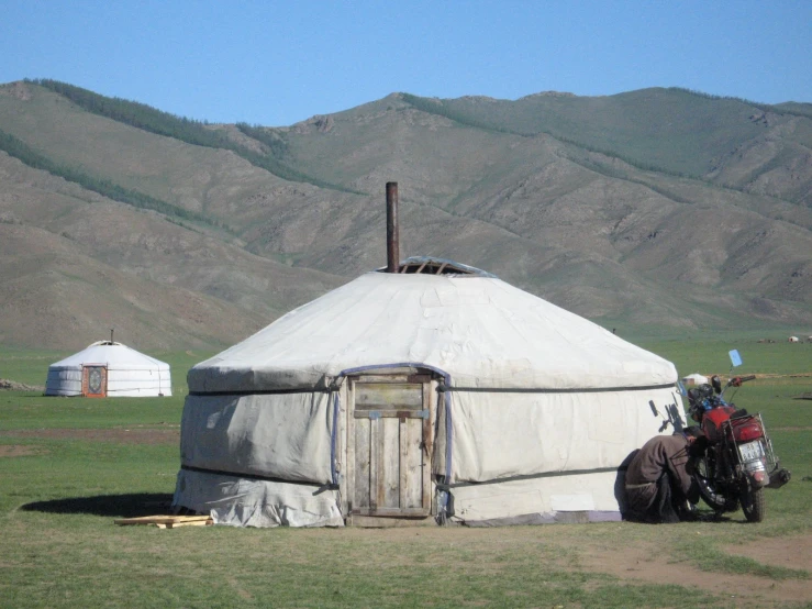 a horse is outside of a ger that is next to mountains