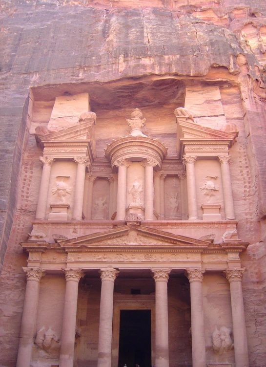 people stand outside an ancient building carved into the side of a mountain