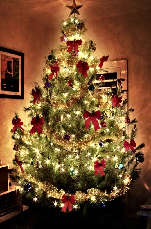 a lit christmas tree is decorated with holiday bows and bells