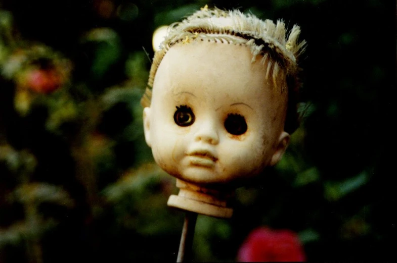 a old doll with some hair is holding a red rose
