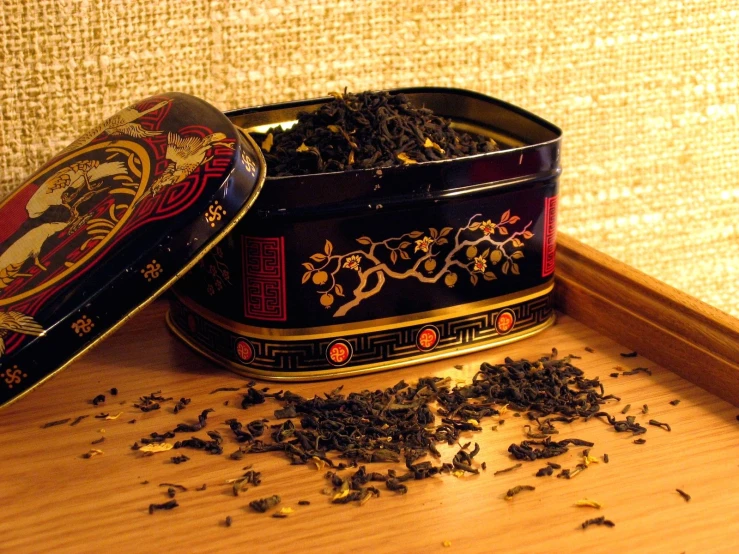 a decorative black container with gold accents next to a pile of leaves and other dried teas