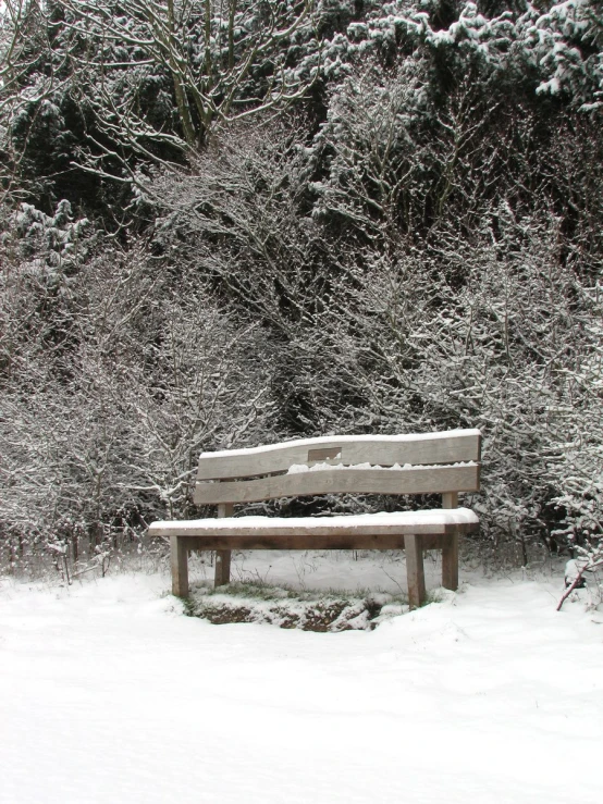 a wooden bench sitting next to some snow covered trees