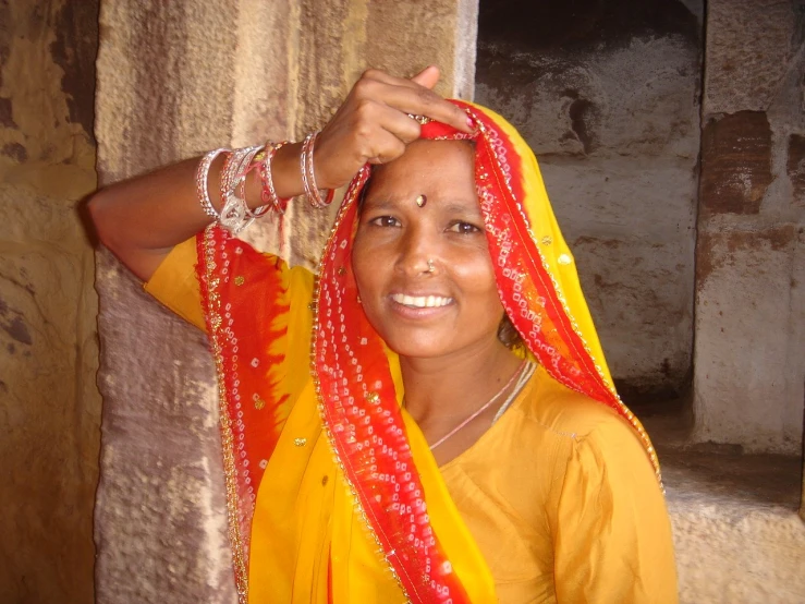 a woman in a yellow and orange sari stands in front of a window