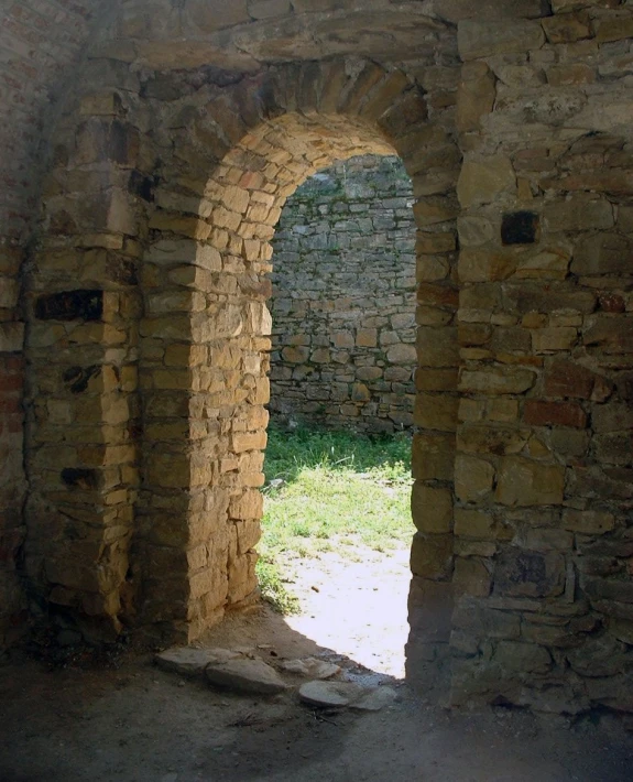 an arch in an old, ruined building leads into a grass field