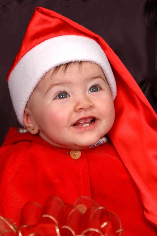 a smiling baby in red clothing with a santa hat