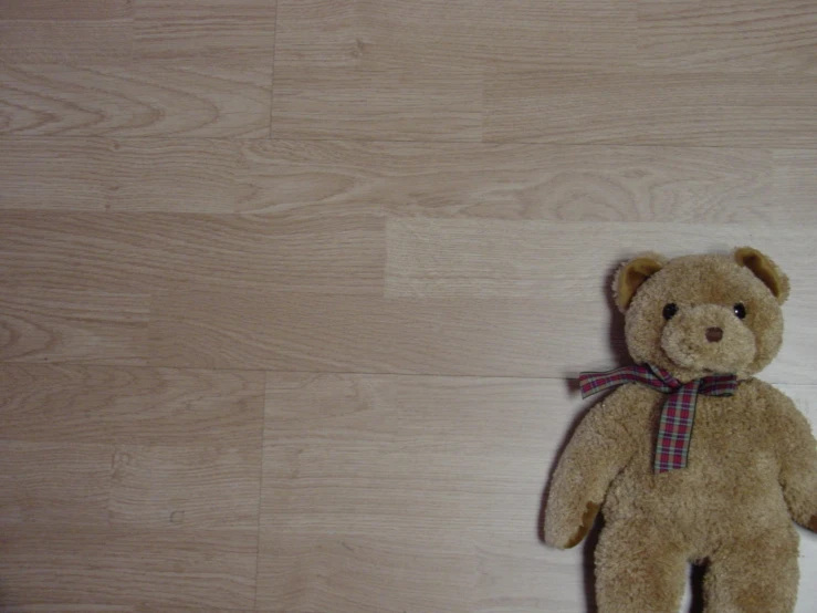 brown teddy bear sitting on top of a wood floor