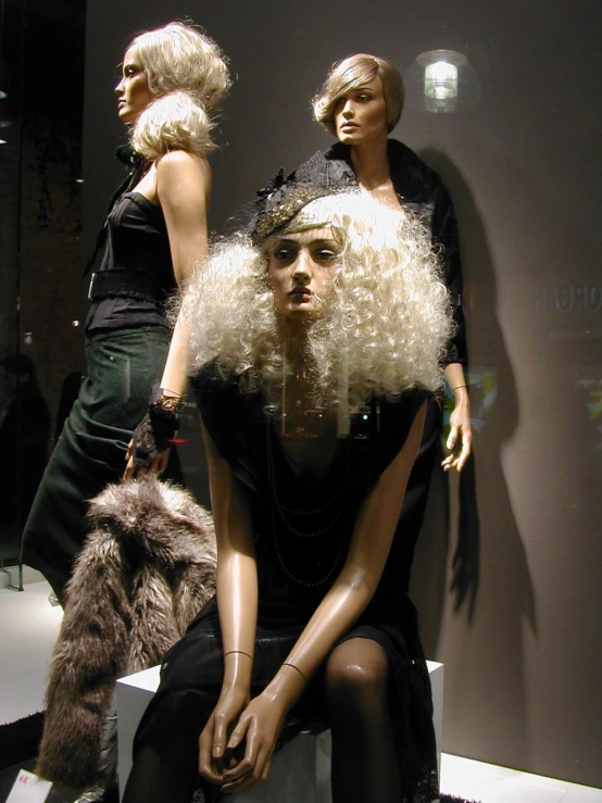 two mannequins sitting on white pedestal, dressed in black clothes and fur