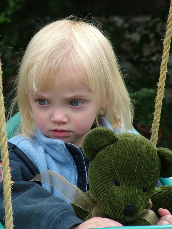 a little girl on a swing with a stuffed bear