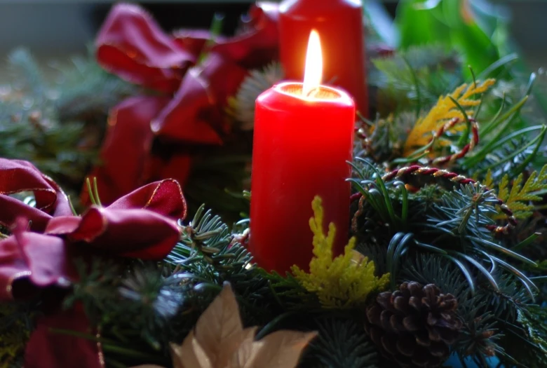 two candles, one lit and two pinecone, surrounded by greenery