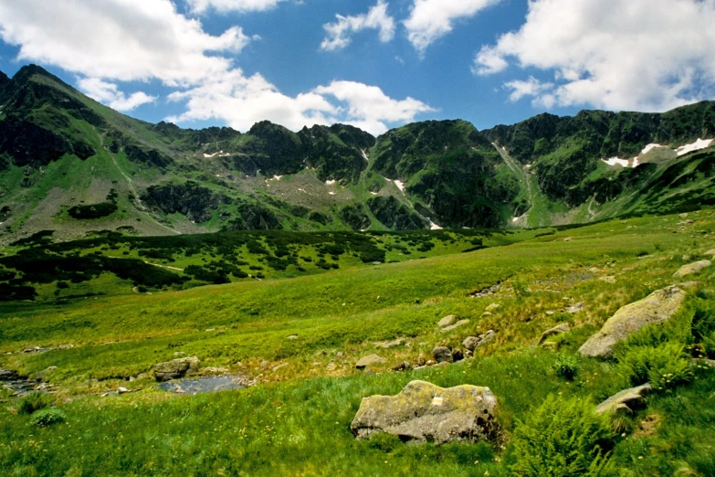 rocky, grassy landscape with mountains and lakes beneath a cloudy sky