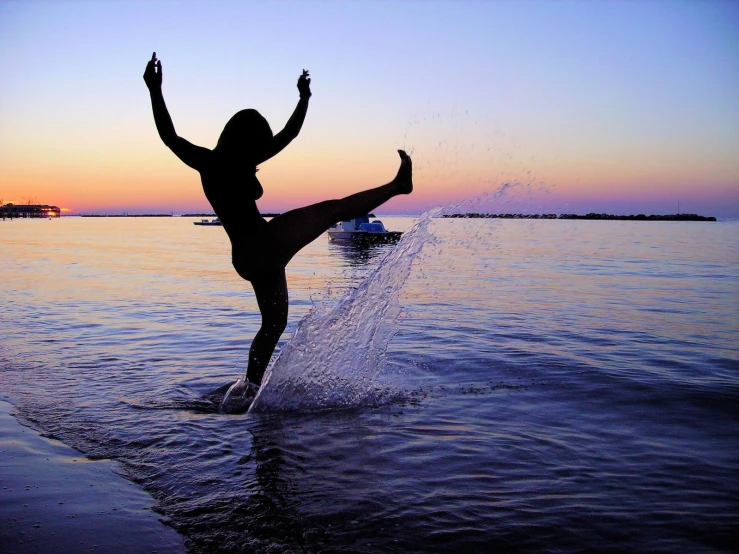 a young woman standing in the water while kicking up soing