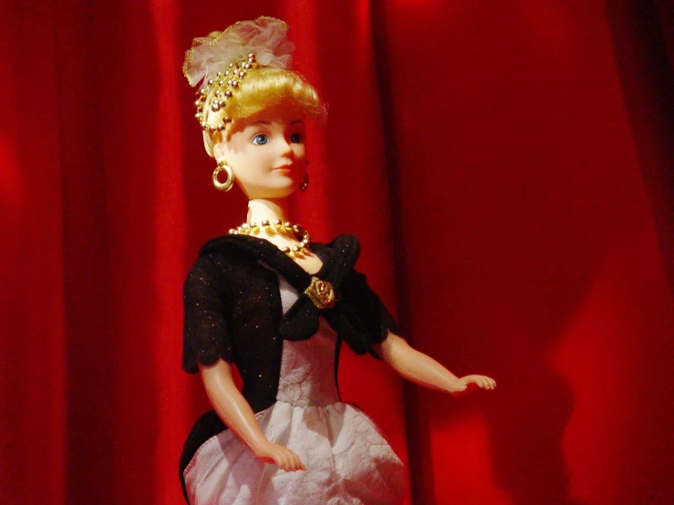 a doll wearing a dress and necklace with a red curtain behind it