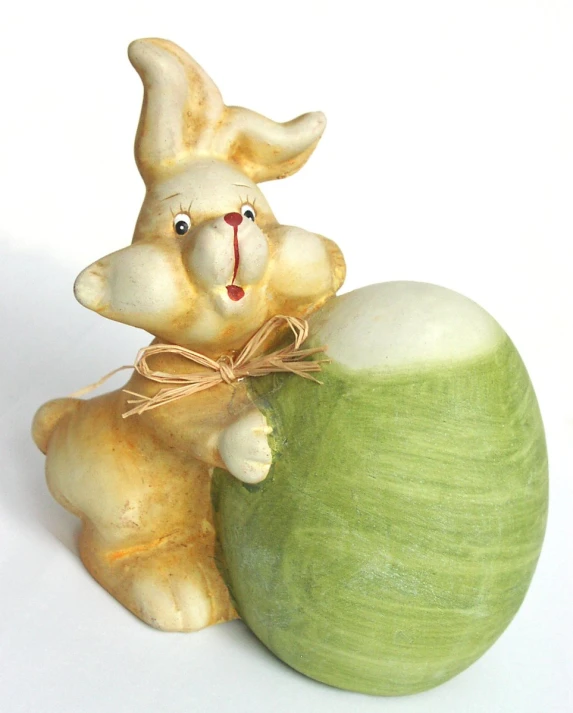 a green and yellow ceramic easter egg with a statue of a bunny carrying an easter basket