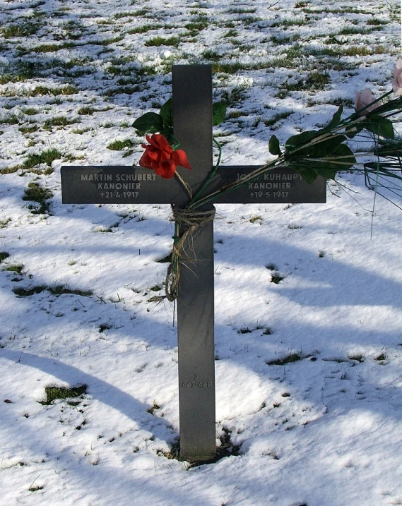 a close up of a small cross in the snow with flowers placed on it