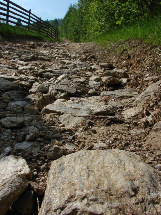 rocky road with a fence and grass on both sides