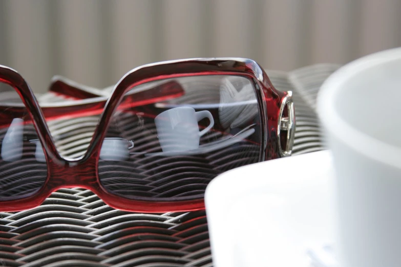 pair of red frames glasses on table next to a white cup