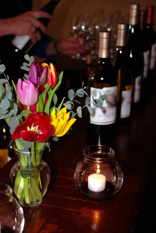 a flower vase with multiple colored tulips in front of a glass of wine