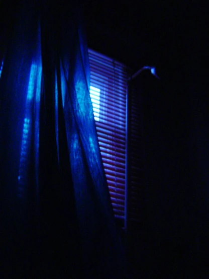 some dark curtains and a lit up window in a darkened room