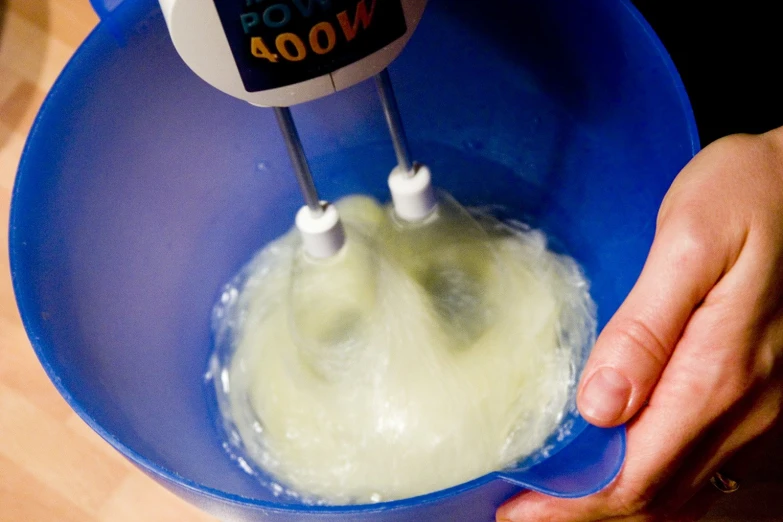 a person stirring a liquid in a blue mixing bowl