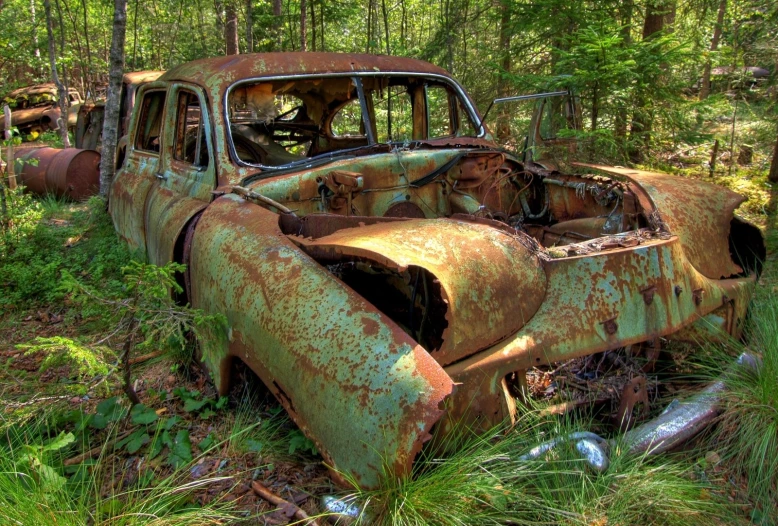 old rusted car in the woods with trees in background