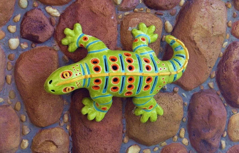 a colorful lizard toy is laying on some rocks