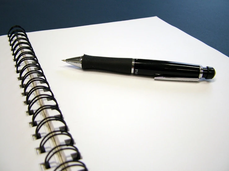 a white spiral notebook next to a black ballpoint pen