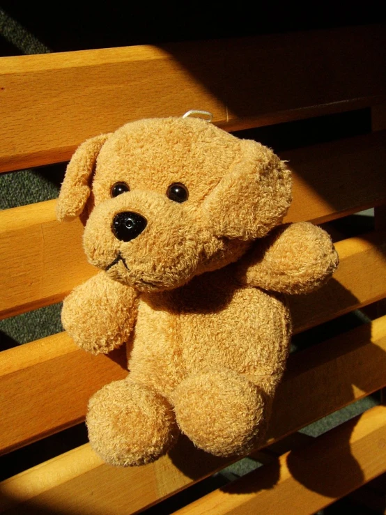 a brown teddy bear sitting on top of a wooden bench