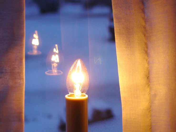 a candle glowing next to a curtain in front of a window