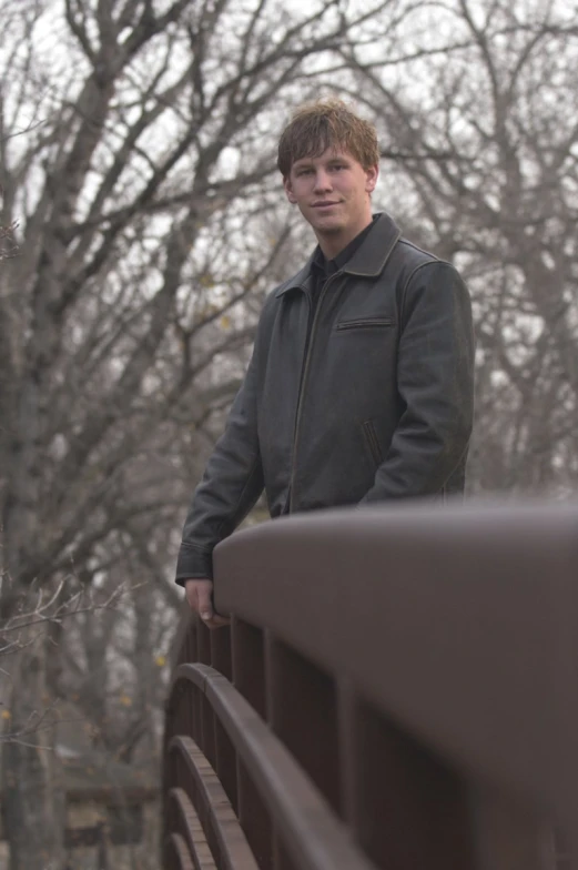 man with coat on posing in front of a bridge