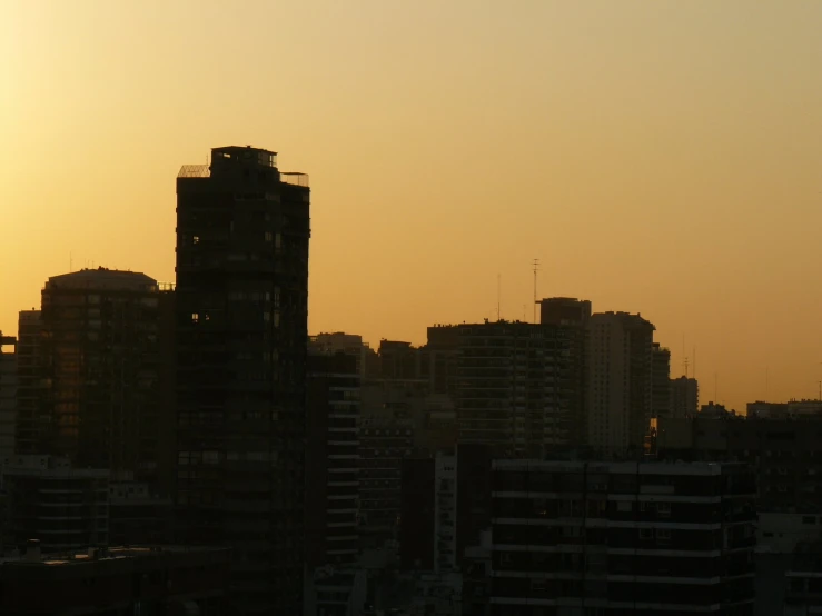 the silhouette of buildings in a city against a yellow sky