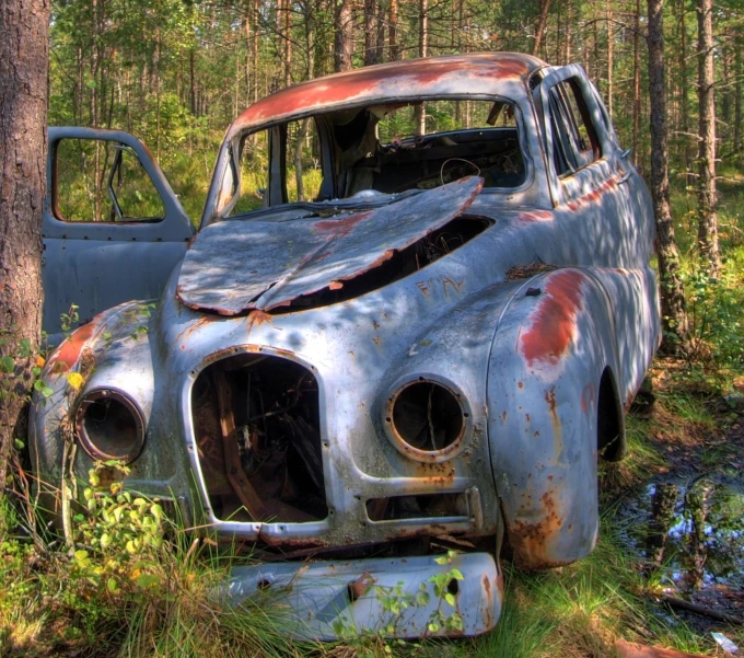 an old rusty car is sitting in the woods