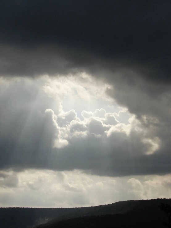 sun breaking through storm clouds above the hills