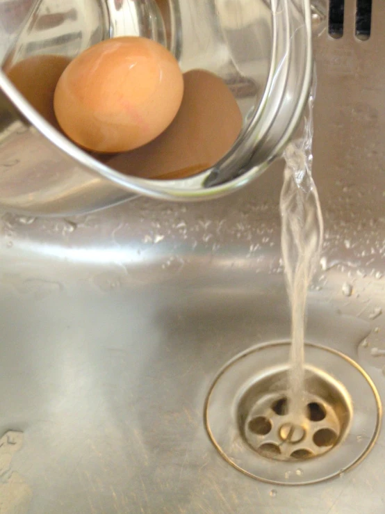 an egg in a metal bowl is being washed in a sink