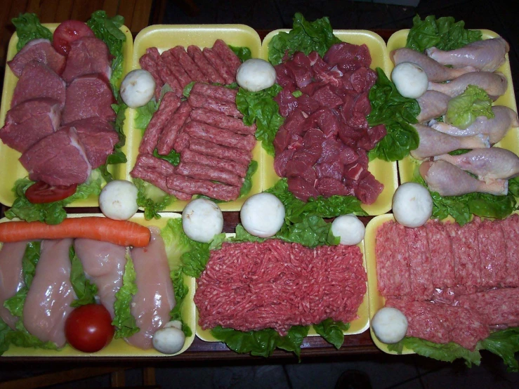 several trays with meats, tomatoes and greens on them