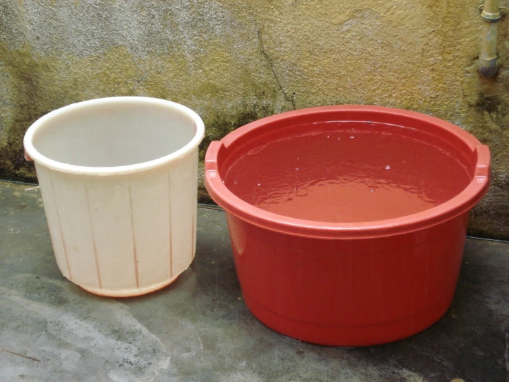 a plastic bucket and a red pot sitting on top of a cement floor