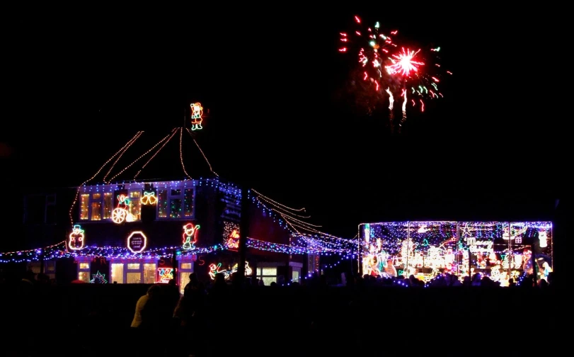 people are standing outside of a home covered in christmas lights