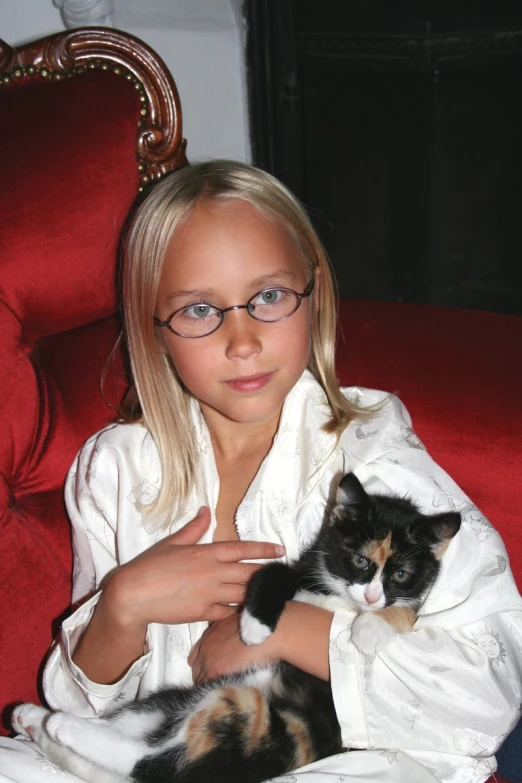 a small blond girl sitting in a chair holding a cat