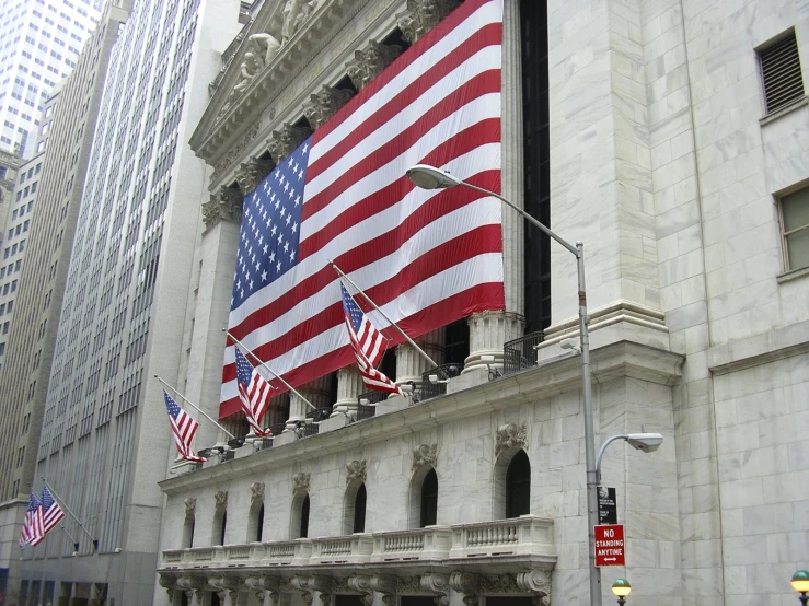 the wall street corner of new york's stock exchange with american flags and other banners hanging from the side of it