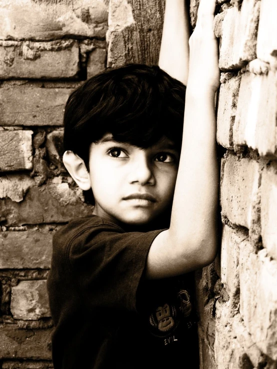 a child with hands over the head leaning against a brick wall