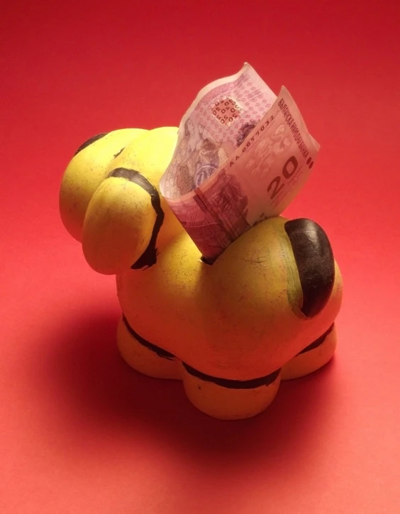 small yellow stuffed toy with one euro bank on red background
