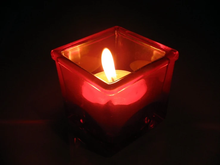 candle glowing brightly in glass square shape at night