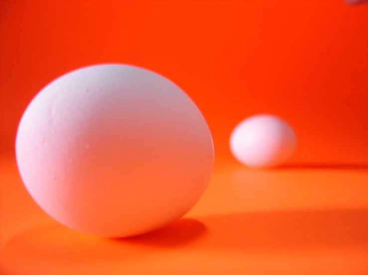 a large and small egg are posed on an orange table