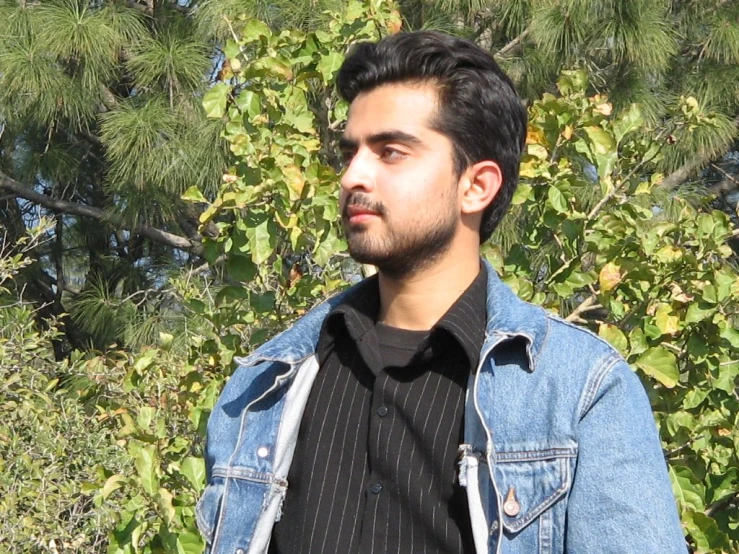 man in a jacket and  shirt, standing next to the trees